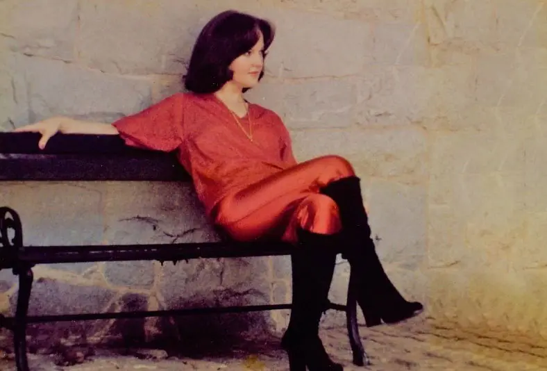 A woman sitting on top of a bench wearing black boots.