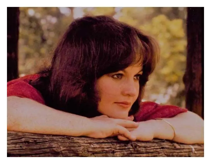 A woman leaning on a wooden bench with her head resting on the arm of it.