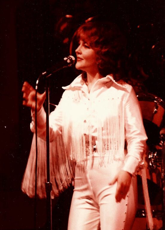A woman in white shirt and pants singing.